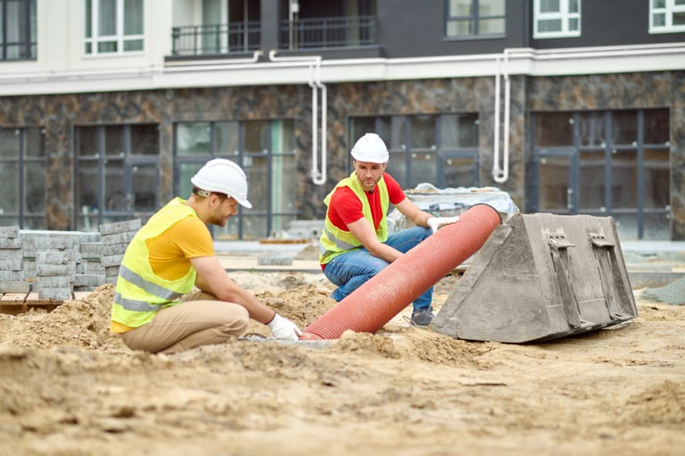 two men crouched near pipe at construction site